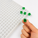 Close-up of an emerald green 1mL cube gummy beside a 736-cavity mold